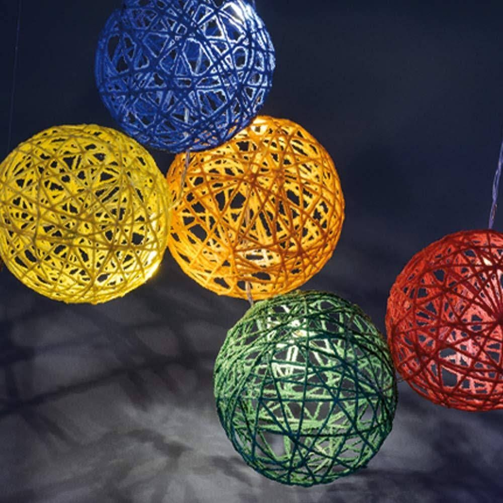 Fünf kugelförmige Wollfadenlampen in Blau, Gelb, Orange, Grün und Rot hängen im Dunkeln.