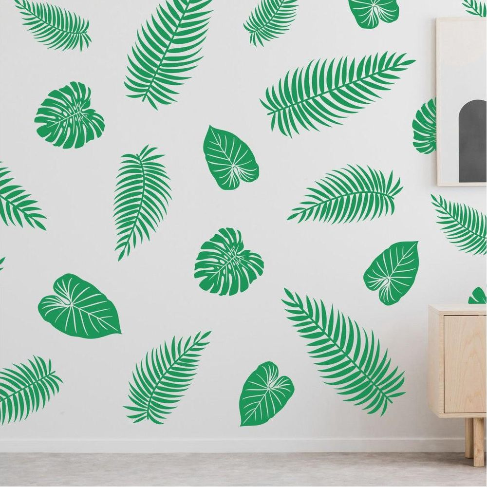 Motivo di foglie verdi su muro bianco, con un piccolo mobiletto in legno a destra.
