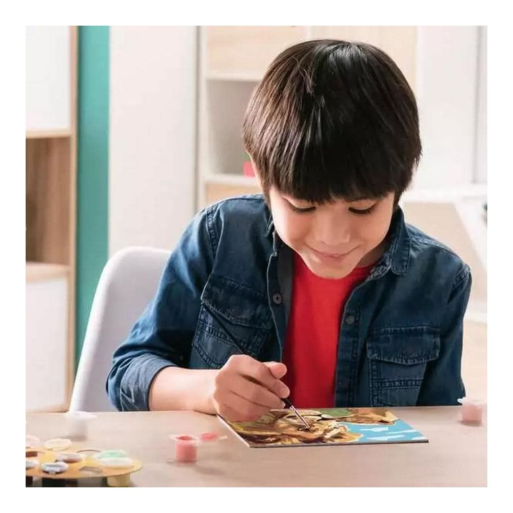 Un niño pinta un cuadro con un pincel y pinturas sobre una mesa.