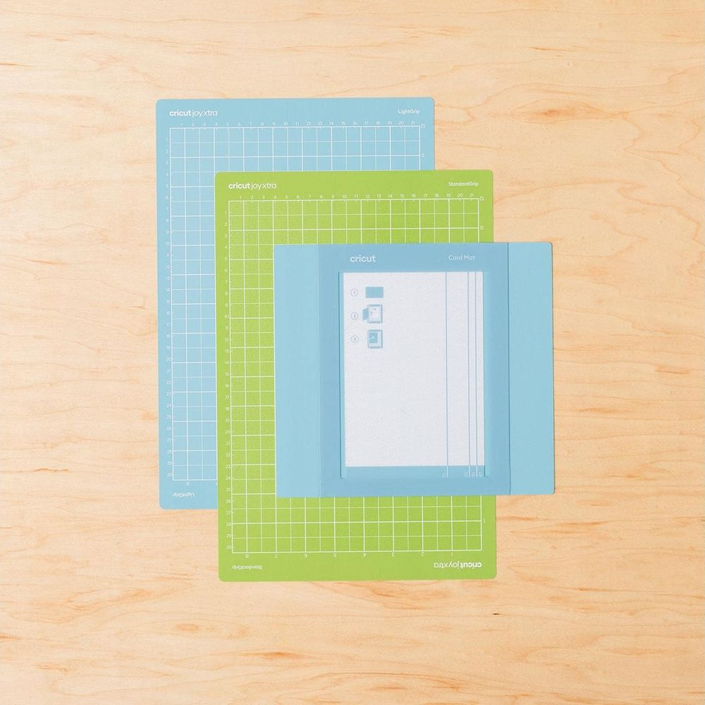 Tres tapetes de corte Cricut en azul, verde y azul claro sobre fondo de madera.