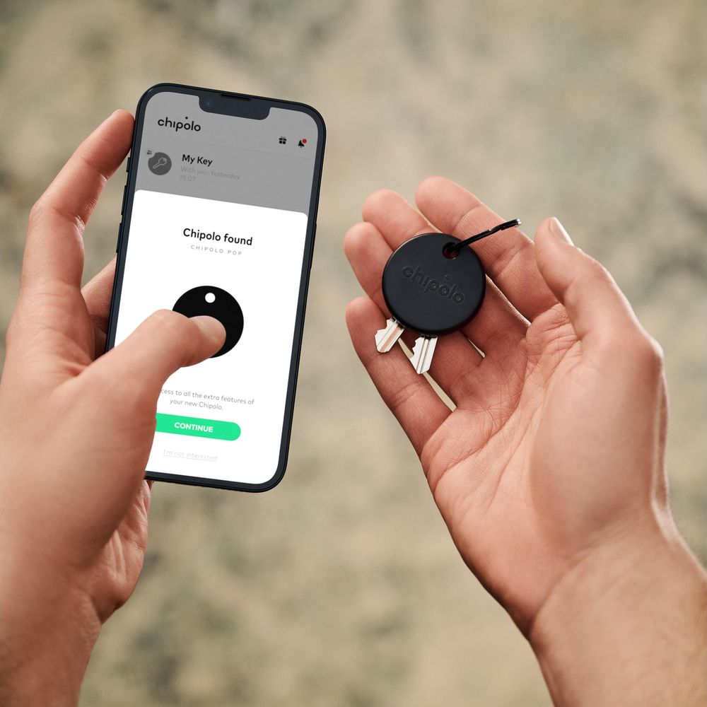 Person holds smartphone with Chipolo app and key fob in hand.
