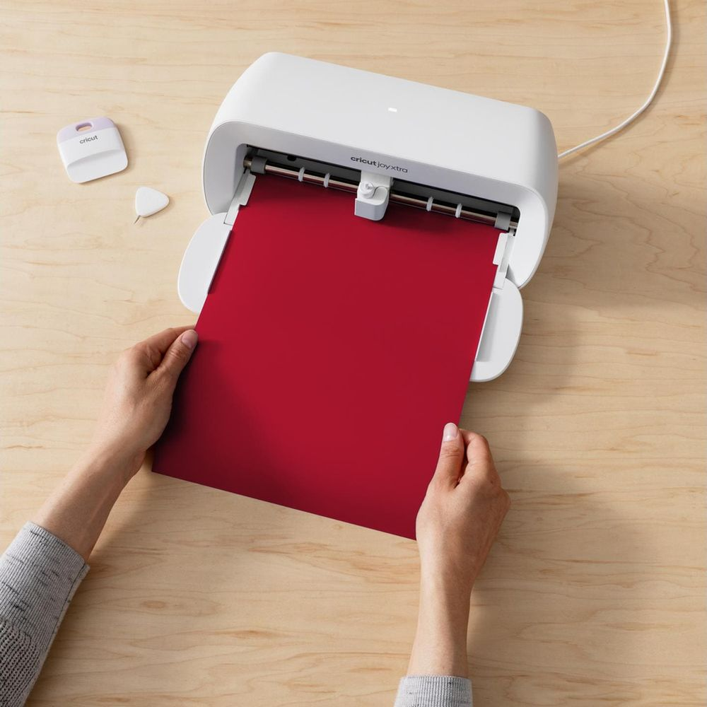 Eine Person setzt ein rotes Blatt Papier in einen weißen Cricut Joy Xtra-Schneideplotter ein.