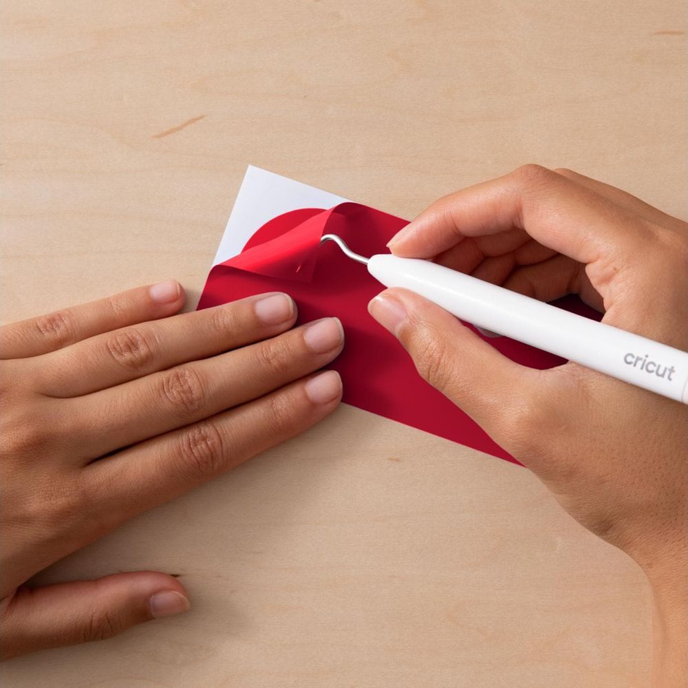 Hände benutzen einen Haken, um rote Folie von weißem Papier abzulösen.