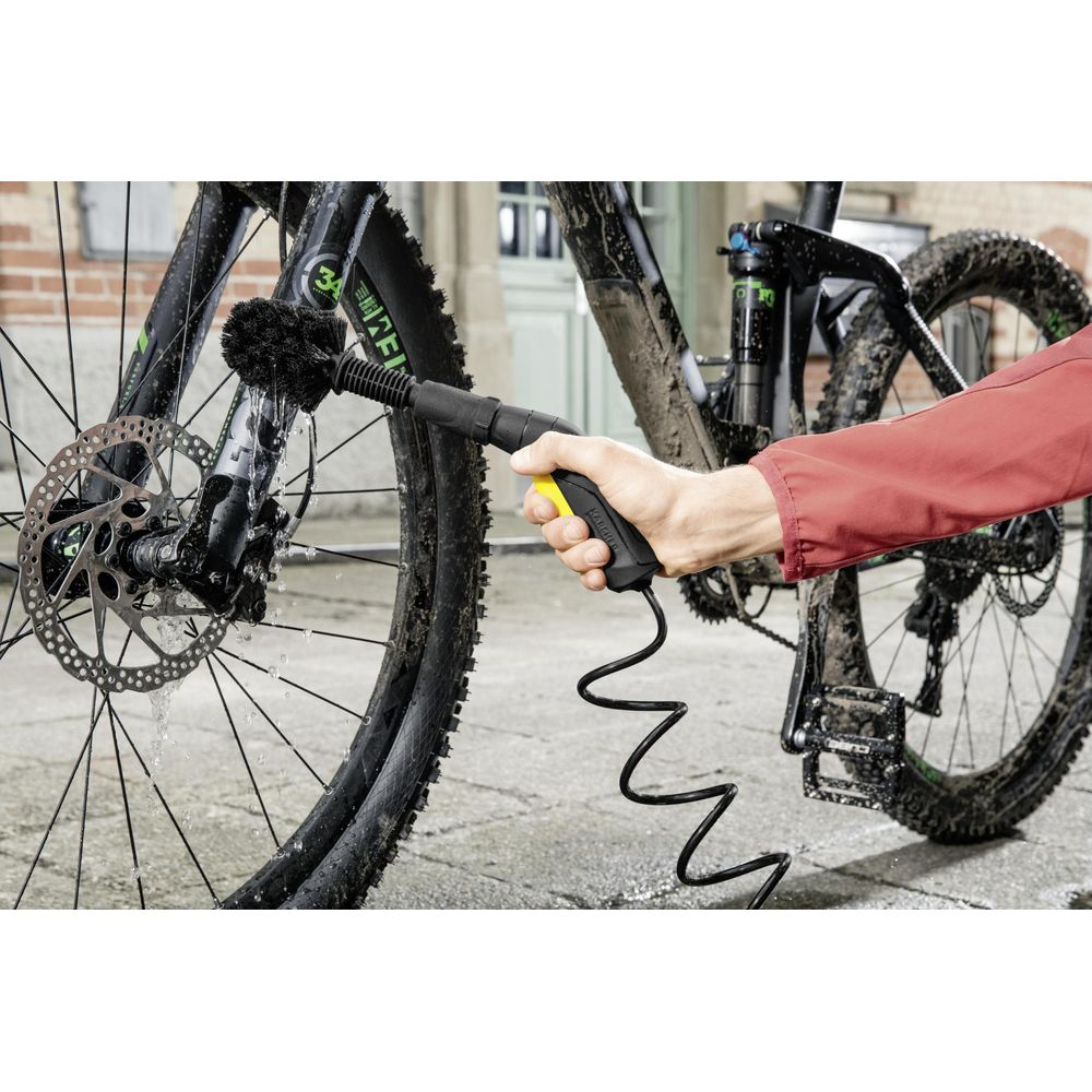 Een hand reinigt een vuile fiets met een borstelhulpstuk.