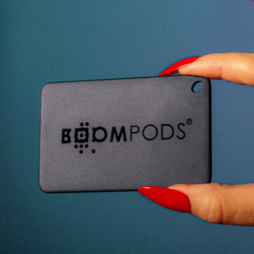 Una mano con unghie rosse tiene un rettangolo scuro con il logo BOOMPOdS.