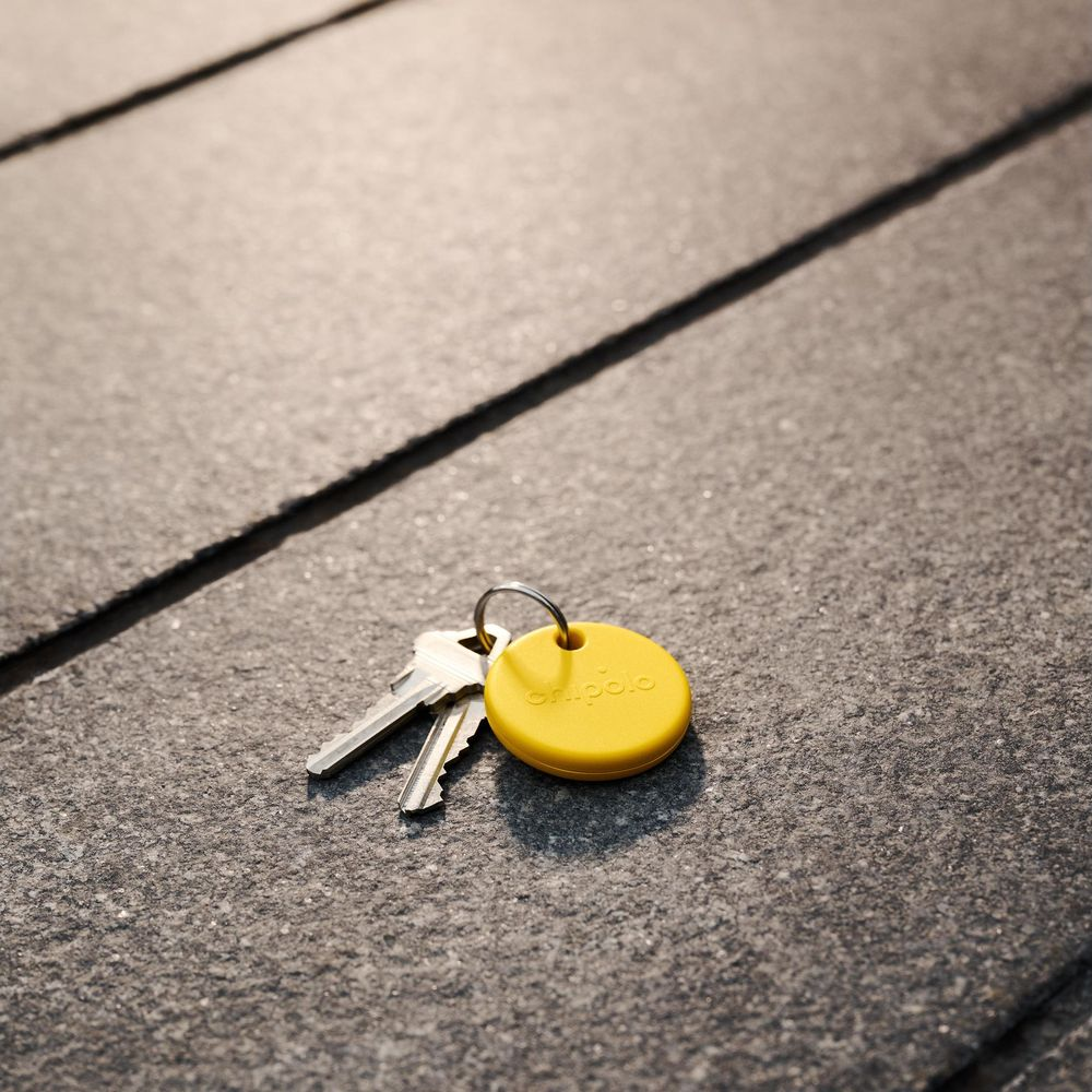 Two keys and a yellow Chipolo tag rest on stone slabs.