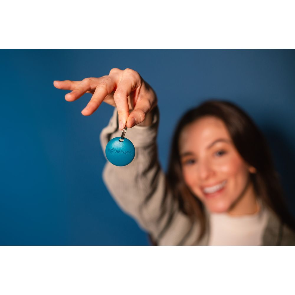 Kobieta trzyma niebieski breloczek z napisem BOOMPODS na niebieskim tle.