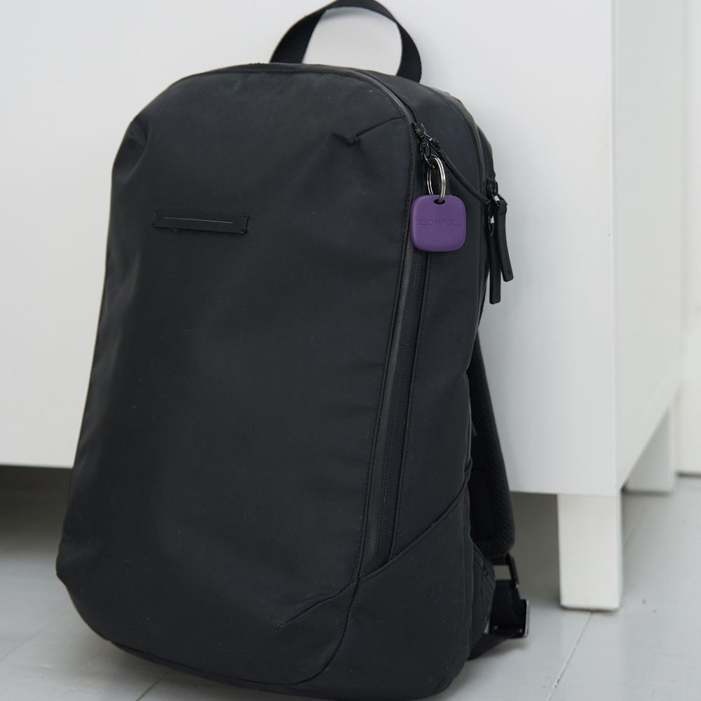 Zaino nero con etichetta viola, su pavimento bianco.