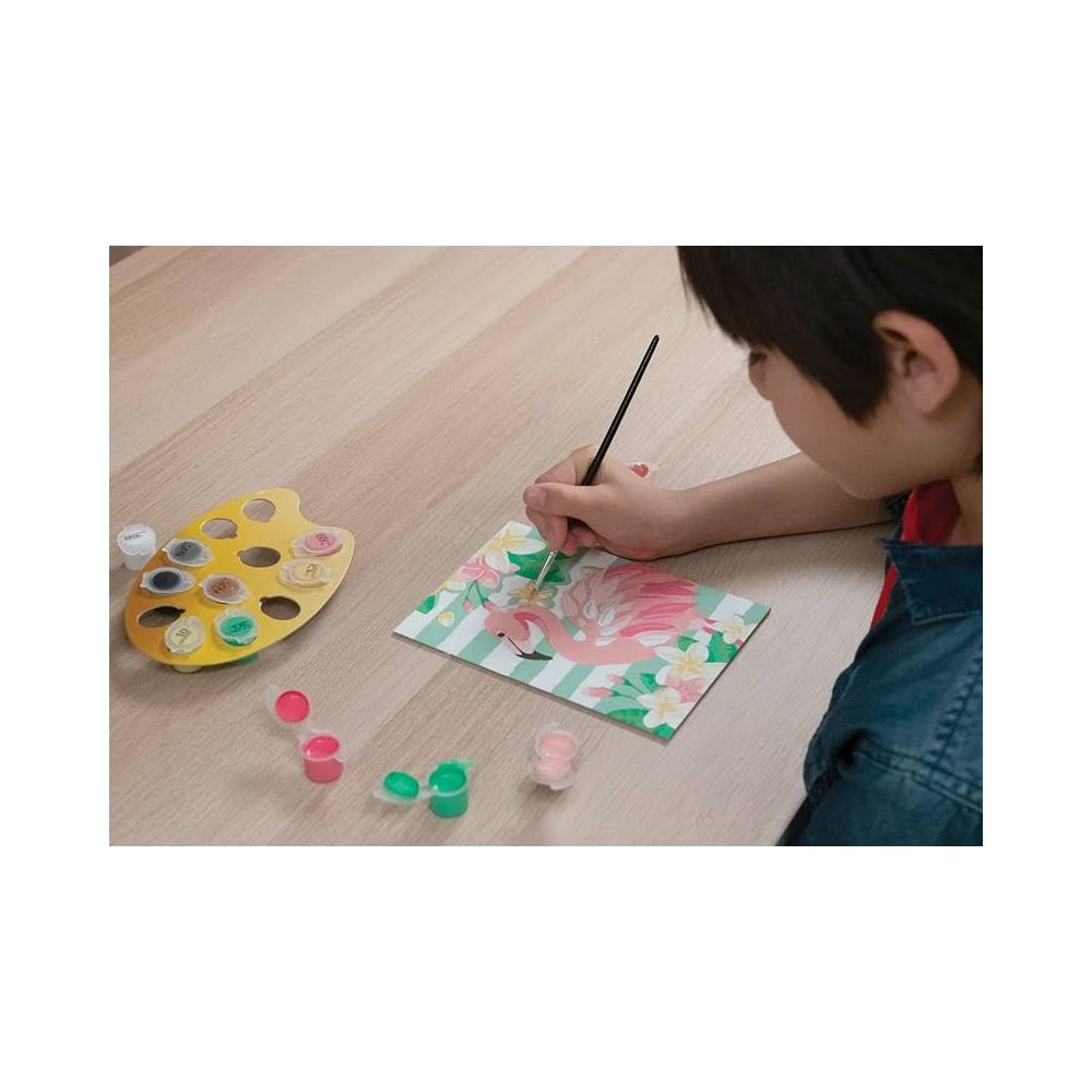 Un niño pinta un flamenco en una tarjeta con pincel y pinturas.