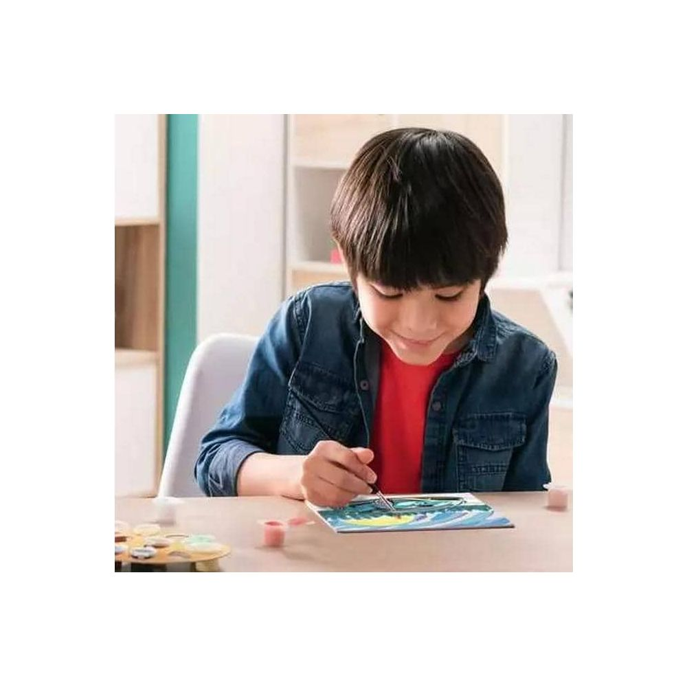 Un ragazzo dipinge un quadro a un tavolo con colori e pennello.