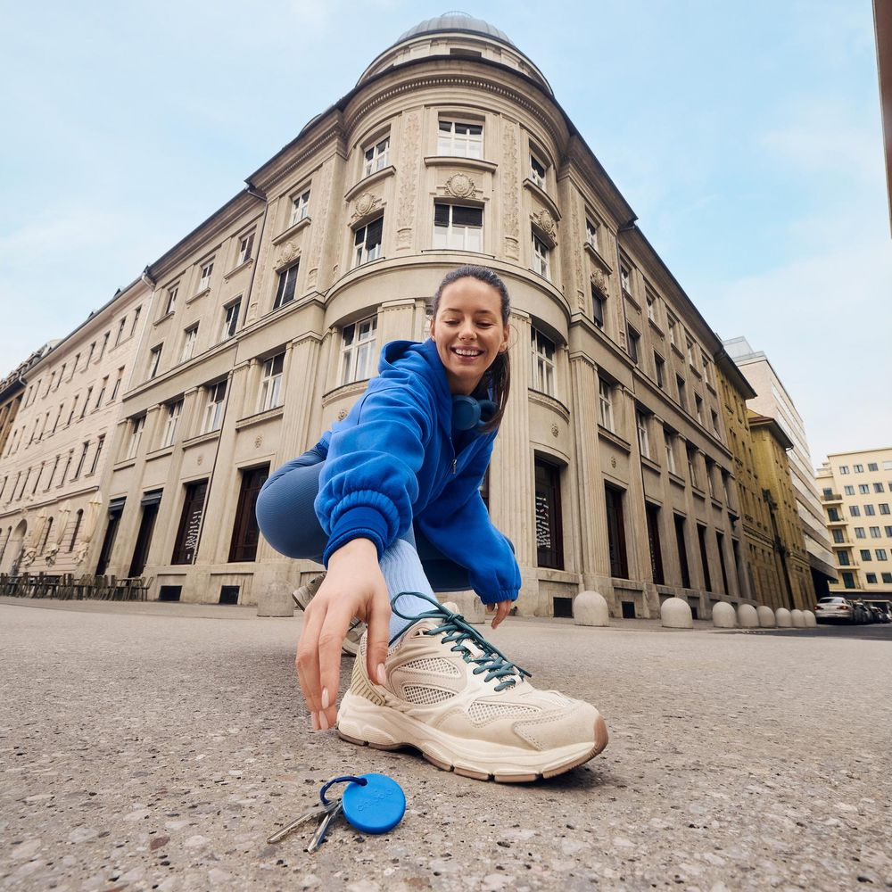 Une femme en sweat à capuche bleu se penche pour ramasser des clés sur le trottoir.