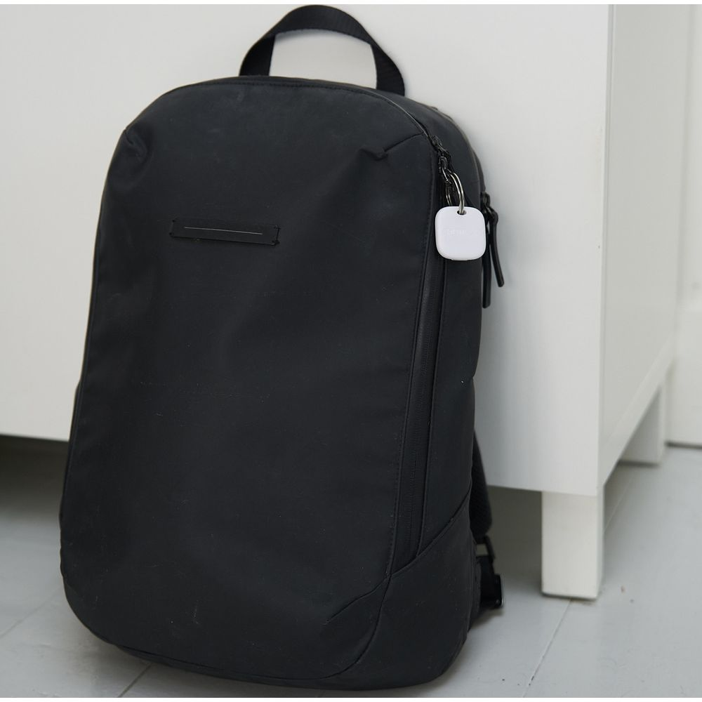 Zaino nero con tracker bianco sulla cerniera, accanto a mobile bianco.