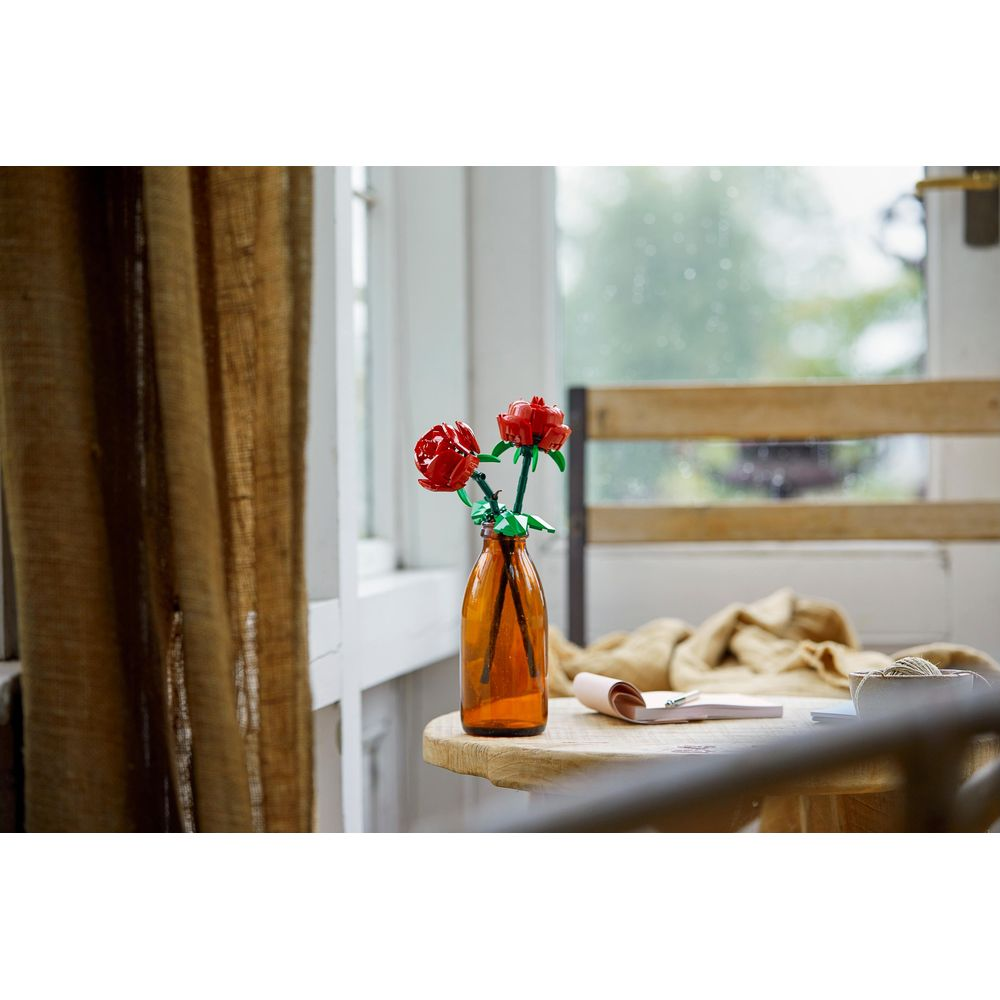 Dos rosas rojas en un jarrón ámbar sobre una mesa de madera.