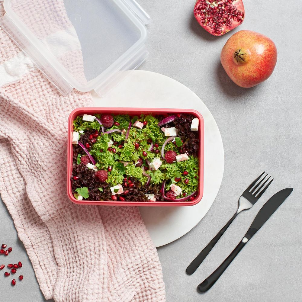 Ein Salat mit Beeren, Granatapfelkernen, Zwiebeln und Feta in einer rosa Schale.
