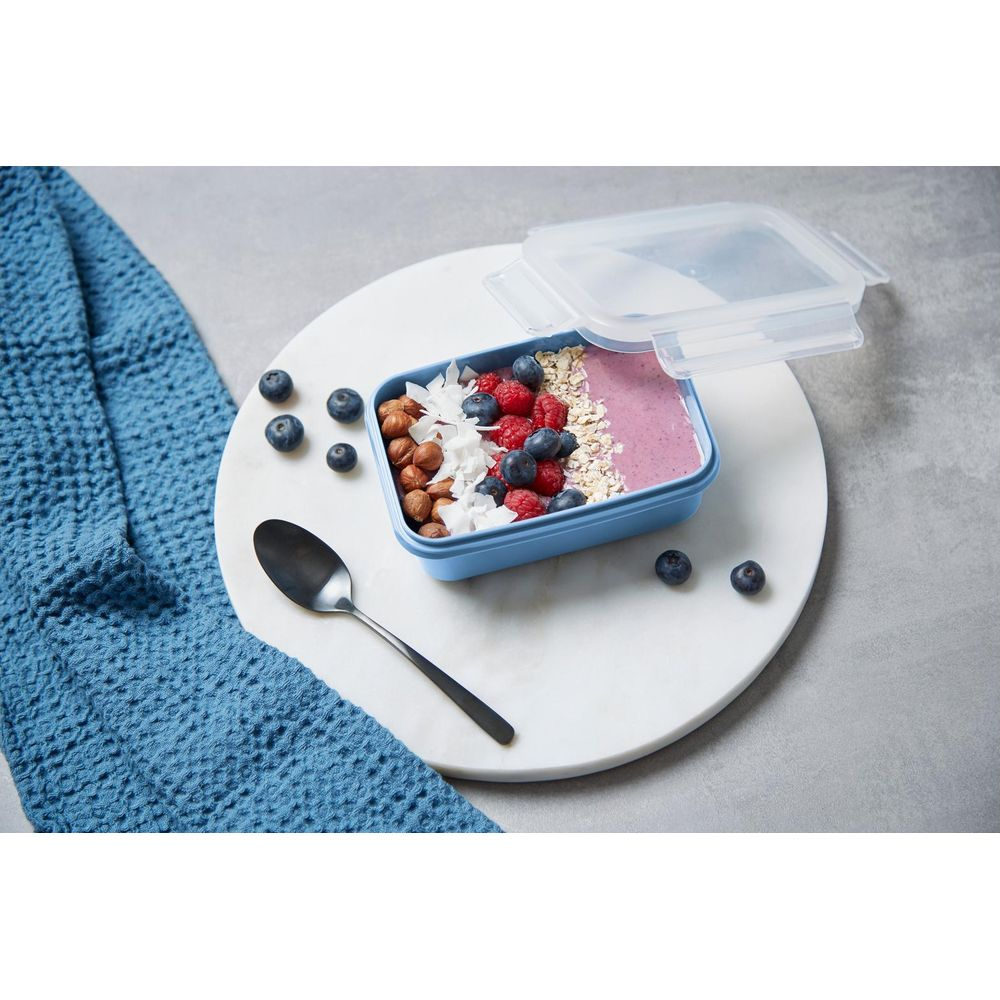 Ein blaues Lunchbox mit Beeren, Nüssen und Haferflocken, daneben ein Löffel.