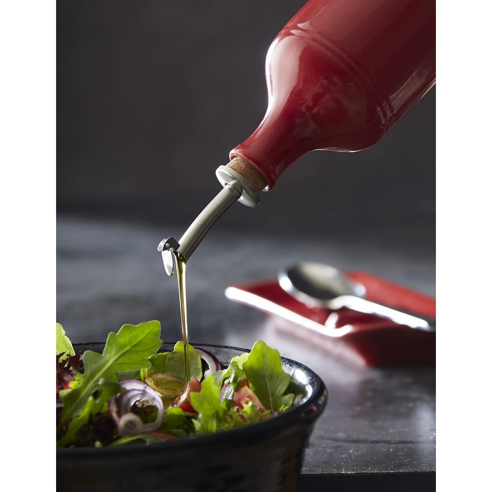 Bottiglia d'olio rossa versa olio in una ciotola di insalata. Cucchiaio vicino.