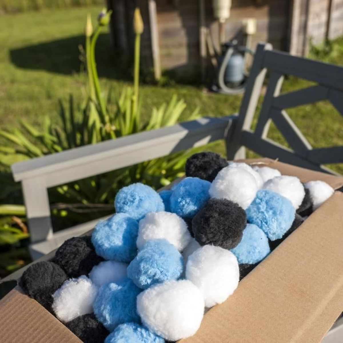 Eine Kiste mit flauschigen Pompons in Schwarz, Weiß und Blau, im Freien auf einer Bank.