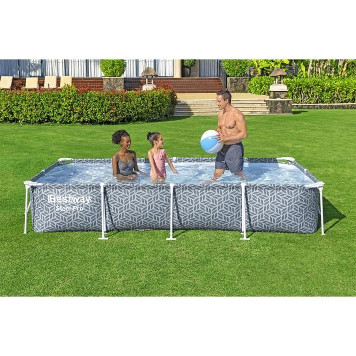 Un homme lance une balle à deux enfants dans une piscine rectangulaire dans un jardin.