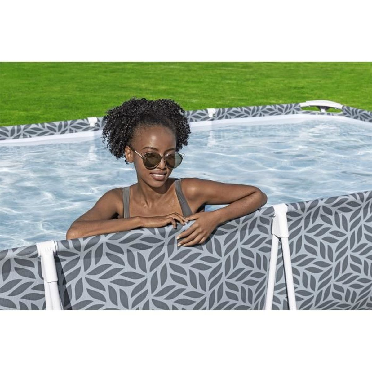 Une femme aux cheveux bouclés foncés avec des lunettes de soleil dans une piscine.