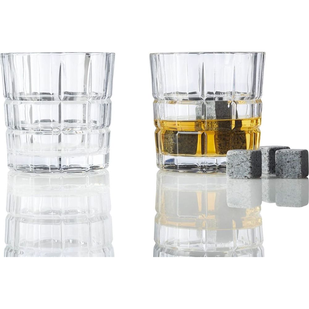 Zwei Glasbecher auf einer spiegelnden Oberfläche. Einer ist leer, der andere enthält Whiskey und drei Steine.