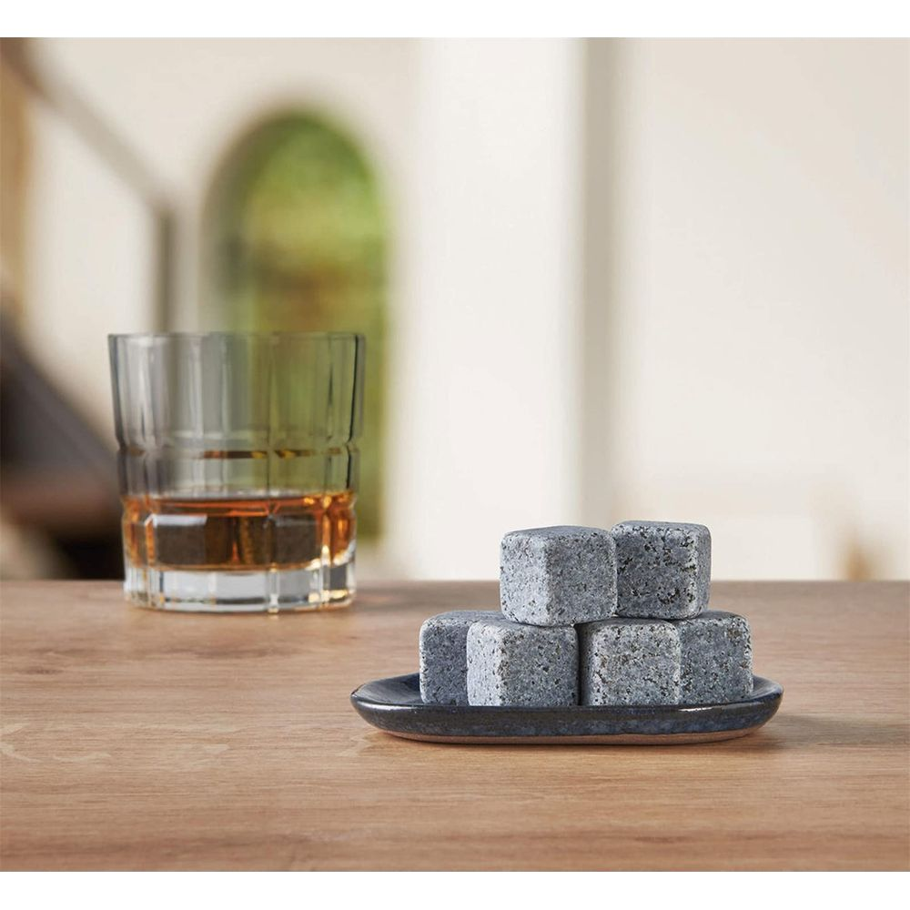 Ein Glas Whisky steht neben einem Stapel Whiskysteinen auf einem Holztisch.