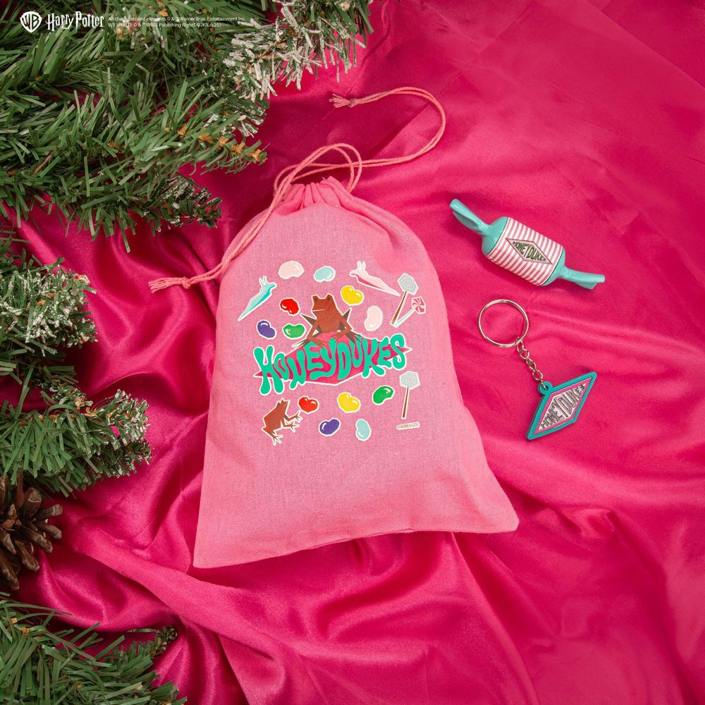 Una bolsa rosa con diseños de Harry Potter, un llavero y dulces al lado.