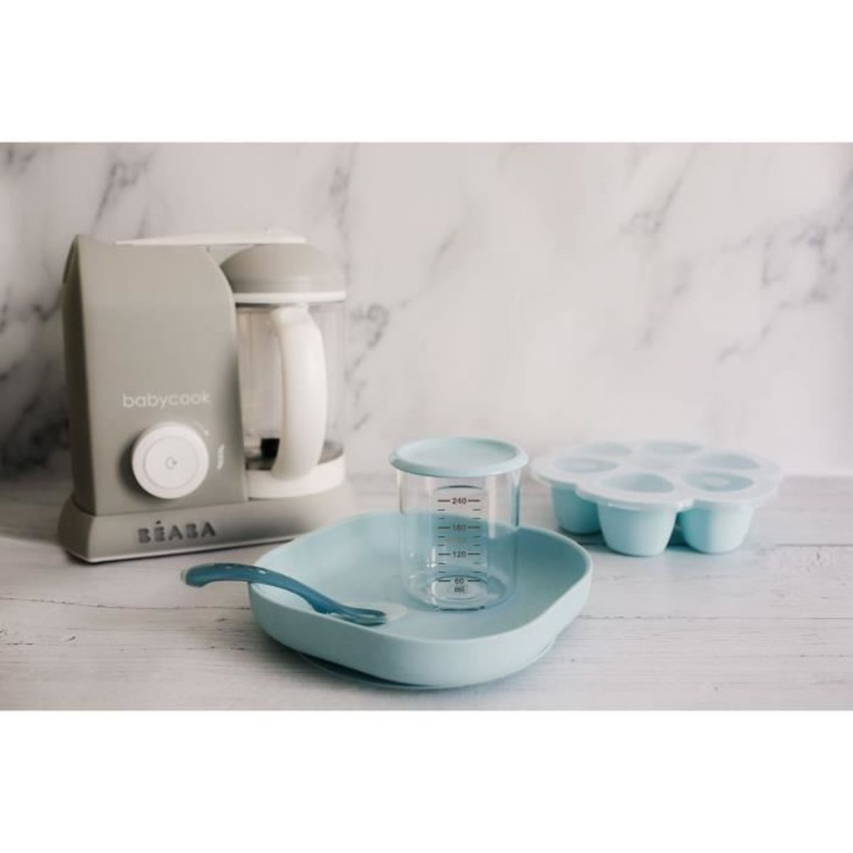 Eine graue Babycook-Küchenmaschine mit einem hellblauen Teller, Becher und Eiswürfelform.