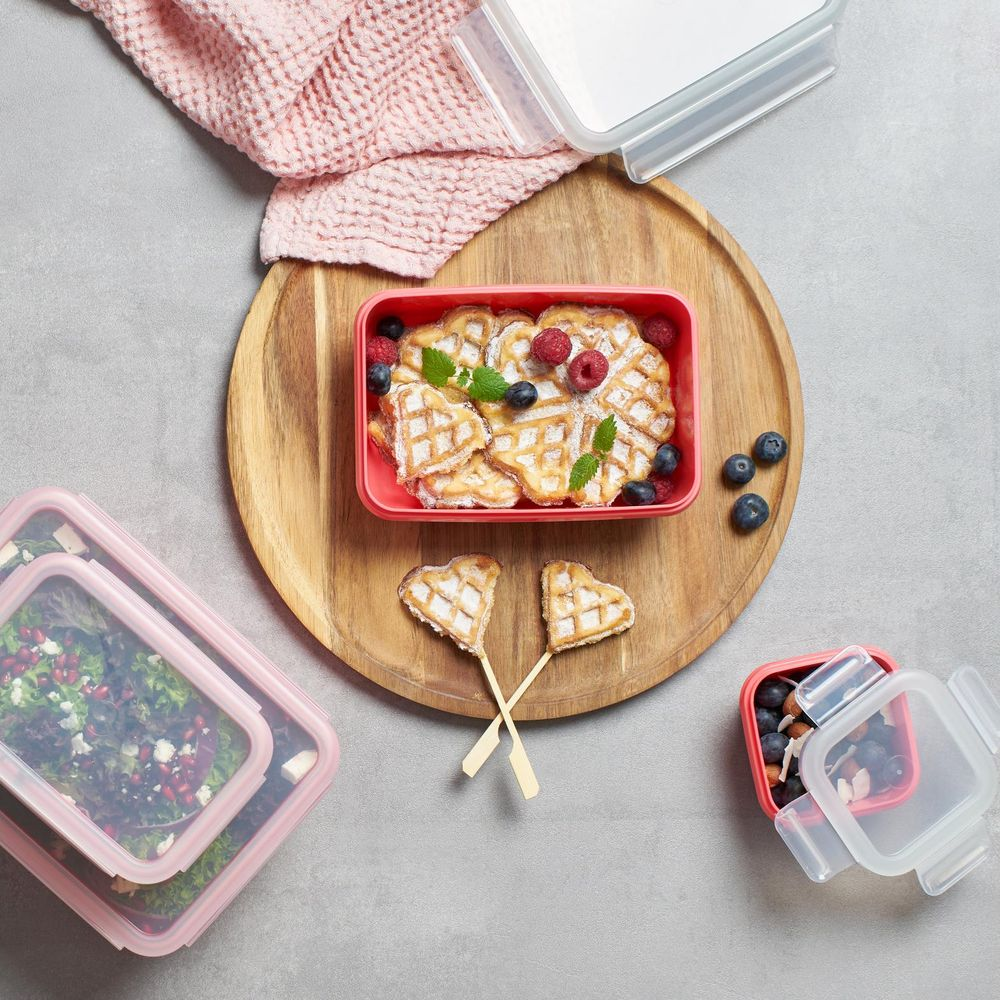 Waffeln mit Beeren in einer roten Schale auf einem Holztablett, daneben Salate.