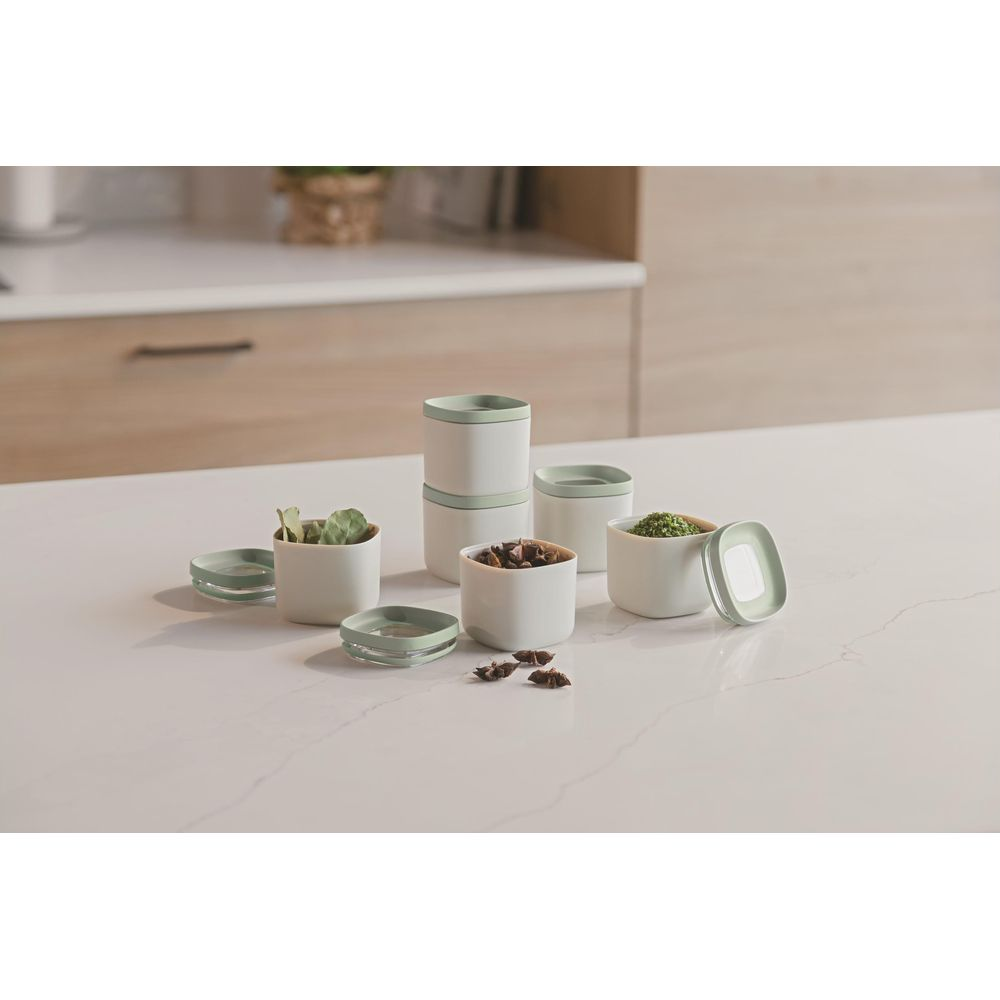 White storage containers with green lids, filled with herbs, spices, and star anise.