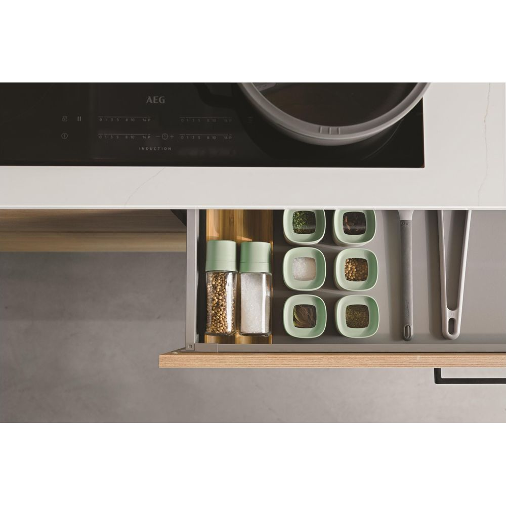 Spice jars and containers in a drawer under an induction cooktop.