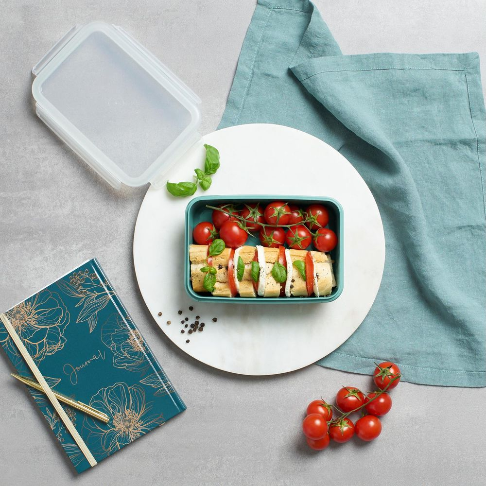 Ein Lunchbox-Set mit Tomaten, Mozzarella, Brot und Basilikum auf einem Marmorteller.