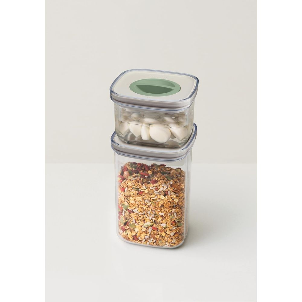 Two stacked food containers: bottom with granola, top with garlic cloves in water.