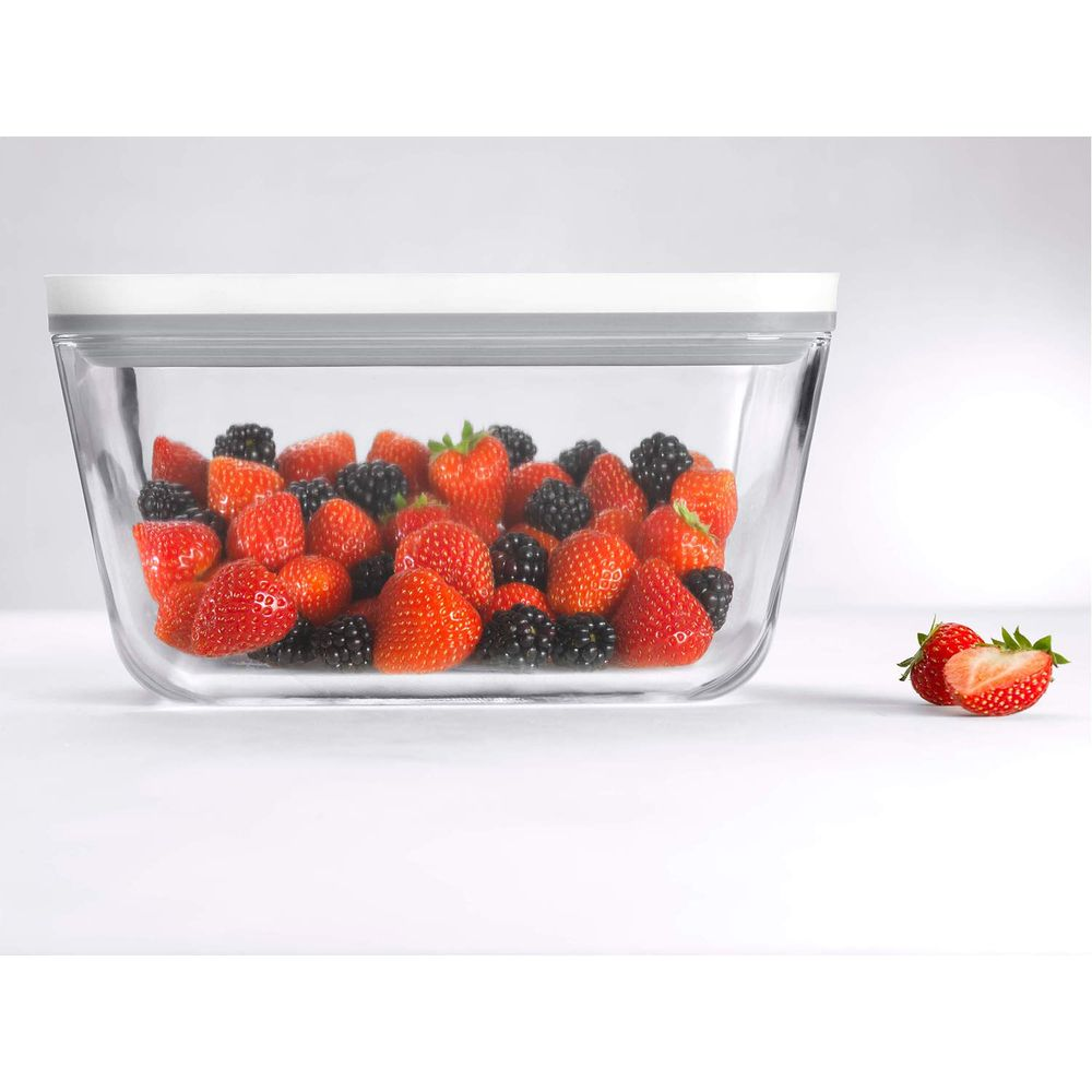 Un recipiente de vidrio lleno de fresas y moras, con dos fresas al lado.