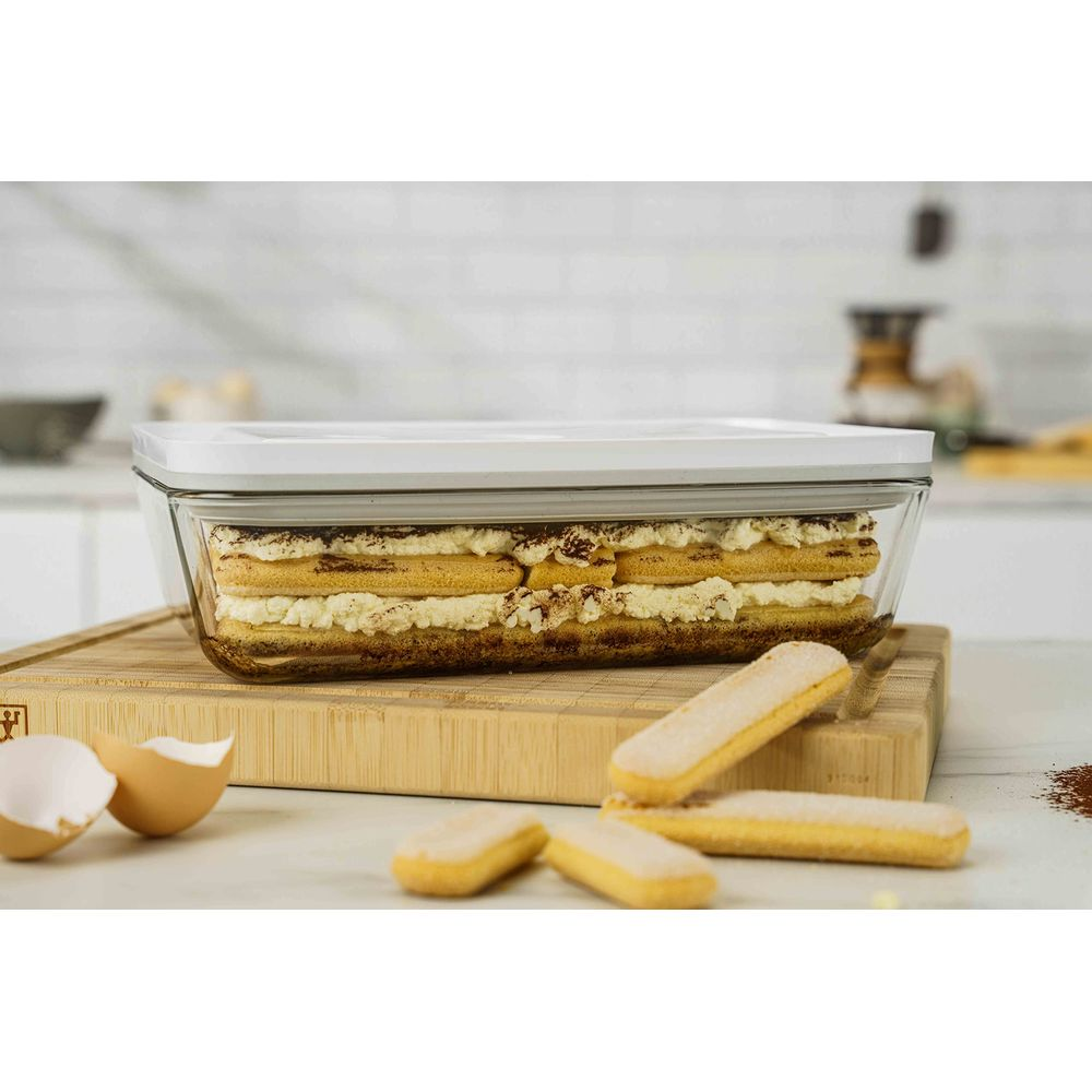 Tiramisu in Glasbehälter auf Holzbrett mit Löffelbiskuits und Eierschalen.