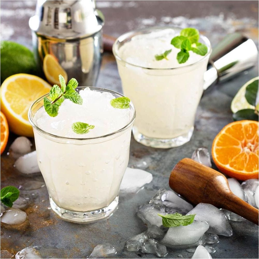Zwei frostige Getränke mit Minze und Zitrusfrüchten, Eis und einem Shaker.