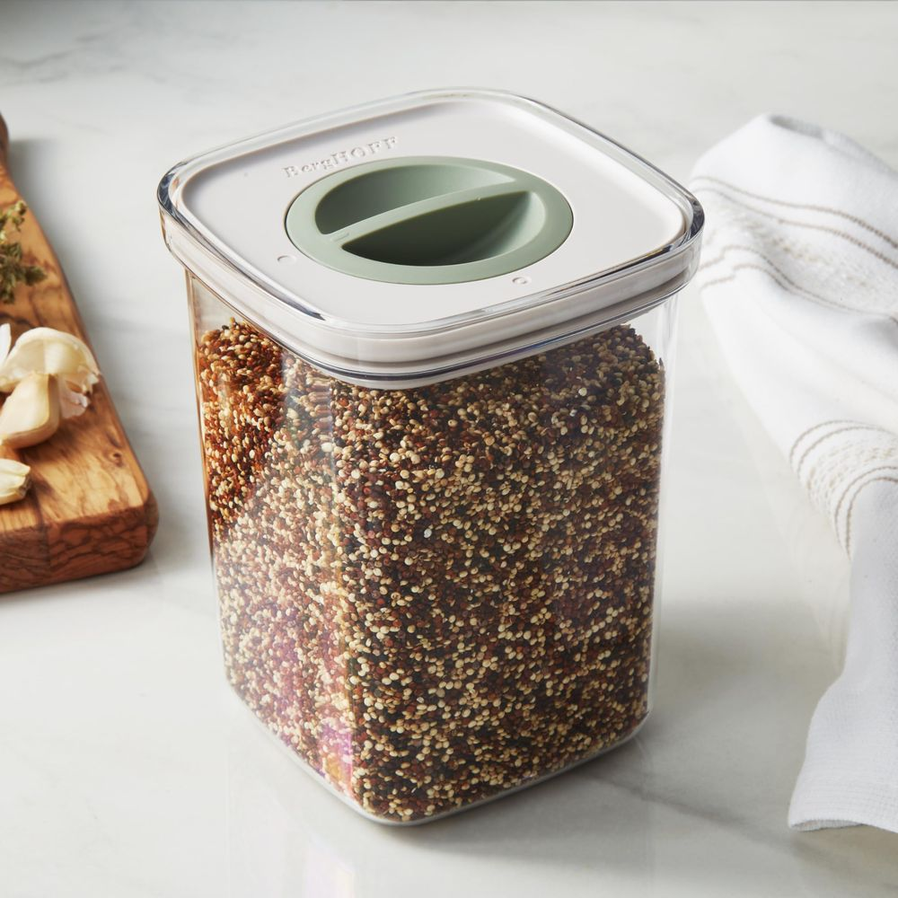 A clear container filled with mixed grains, next to garlic and a towel.