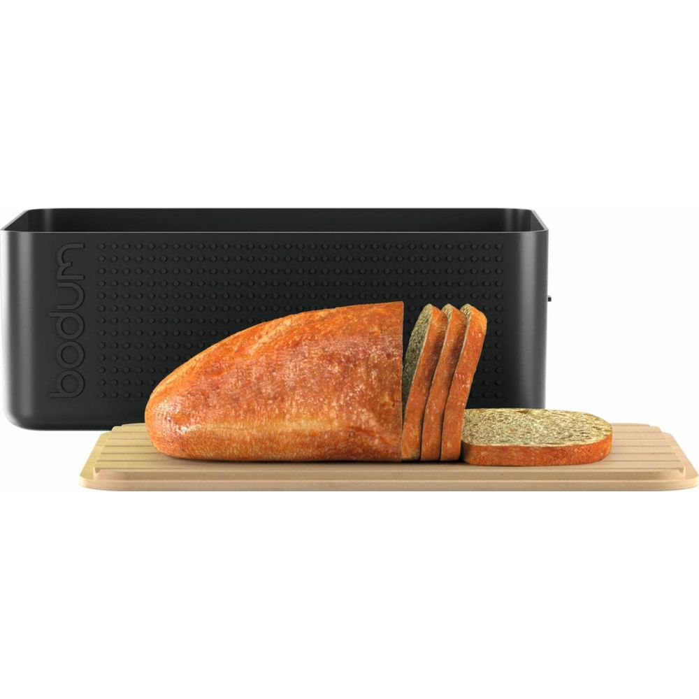 Ein angeschnittener Laib Brot auf einem Holzbrett vor einem schwarzen Brotkasten.