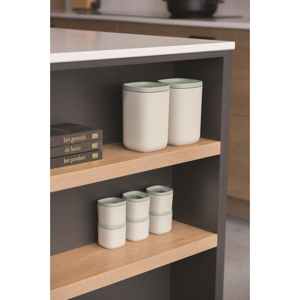 White cups with light green lids on a wooden shelf next to books.