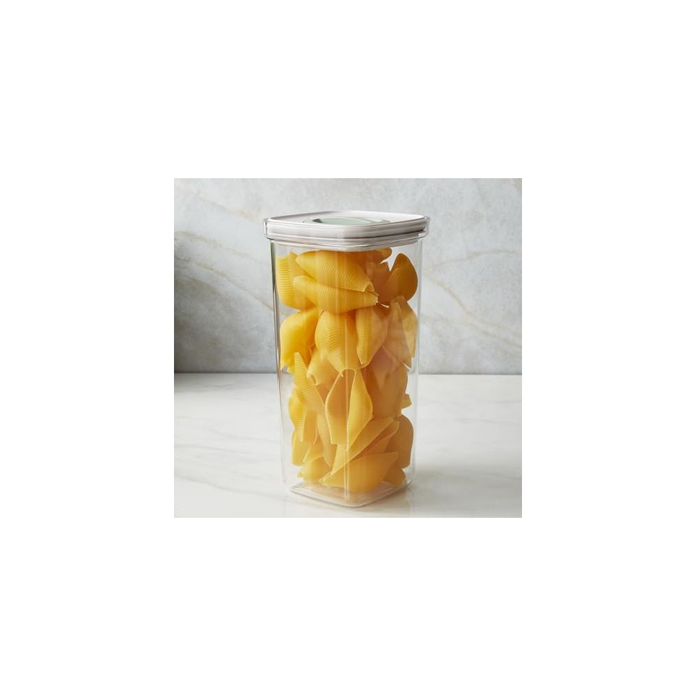 A clear container filled with yellow conchiglie pasta on a marble surface.