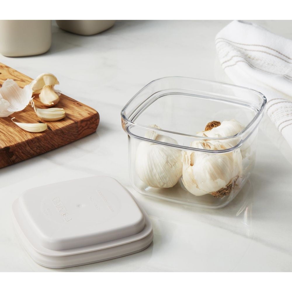 Garlic bulbs in a clear container and on a wooden board. A lid sits nearby.