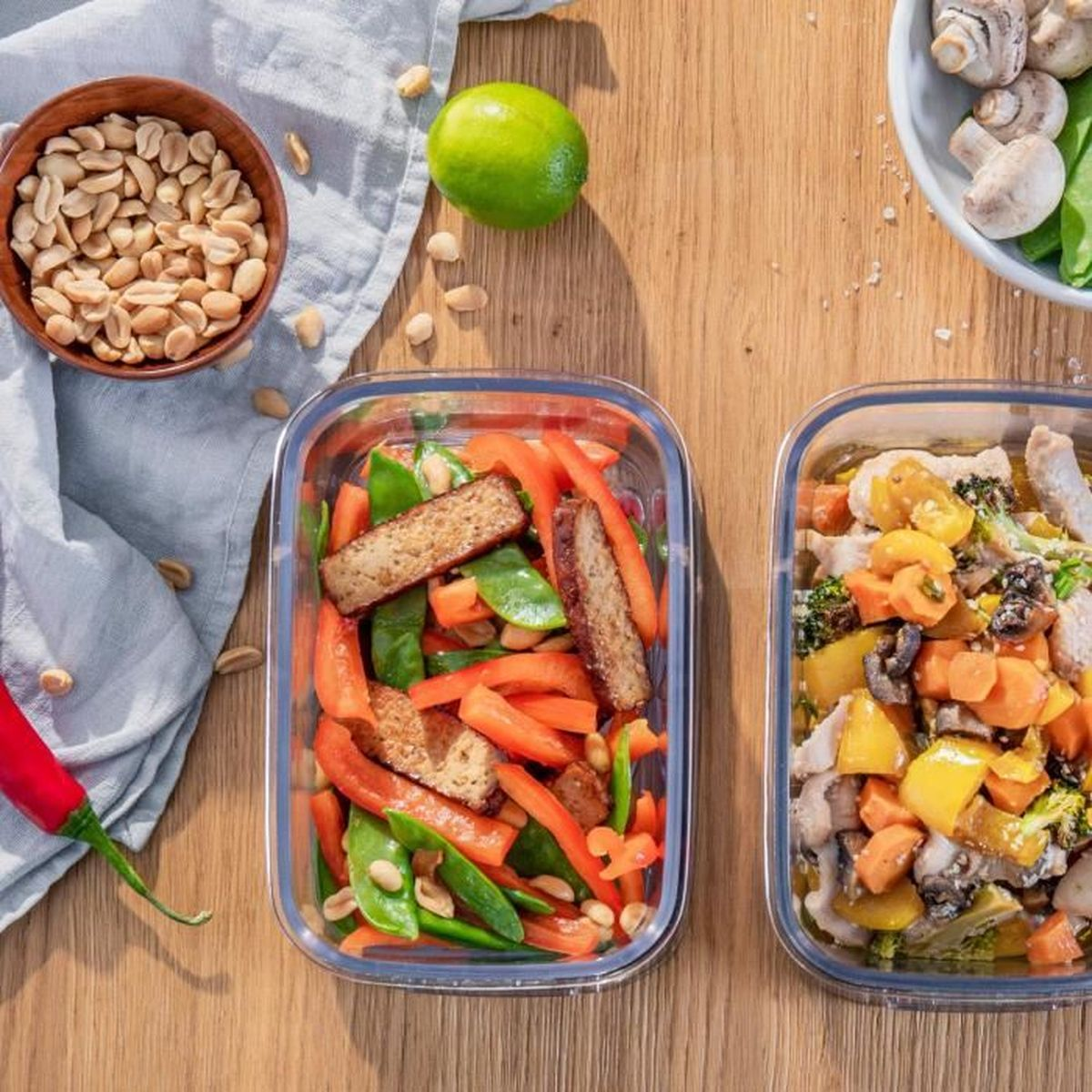 Zwei Behälter mit Essen: einer mit Tofu, Erbsen und Paprika, der andere mit Hühnchen und Gemüse.