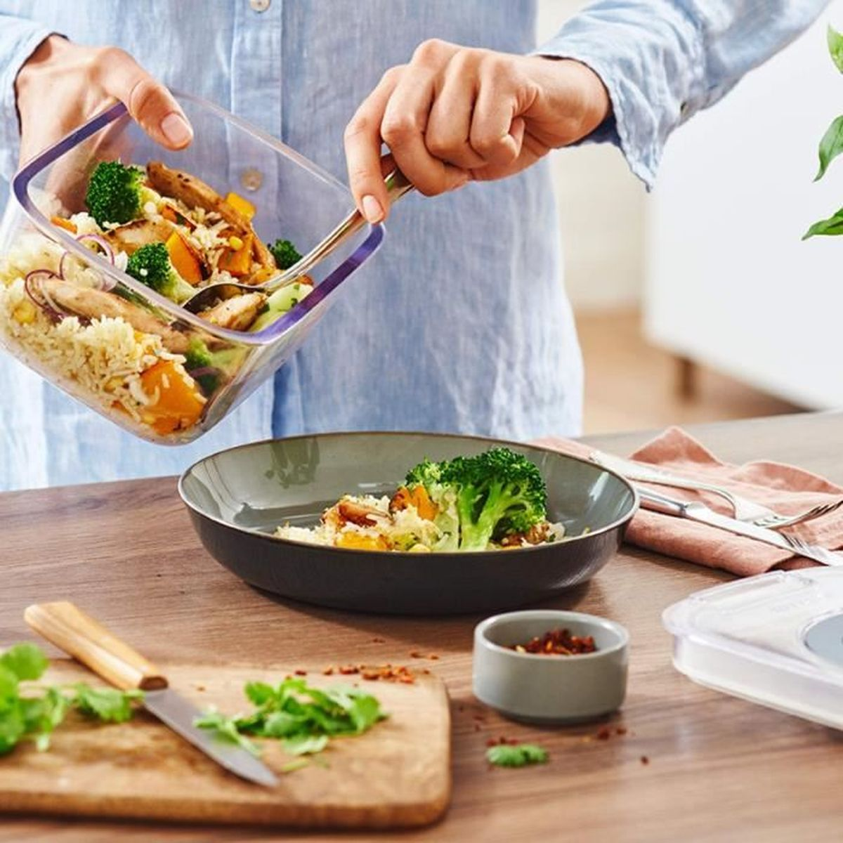 Eine Person schichtet eine Mahlzeit aus Reis, Brokkoli und Hühnchen in eine Schüssel.