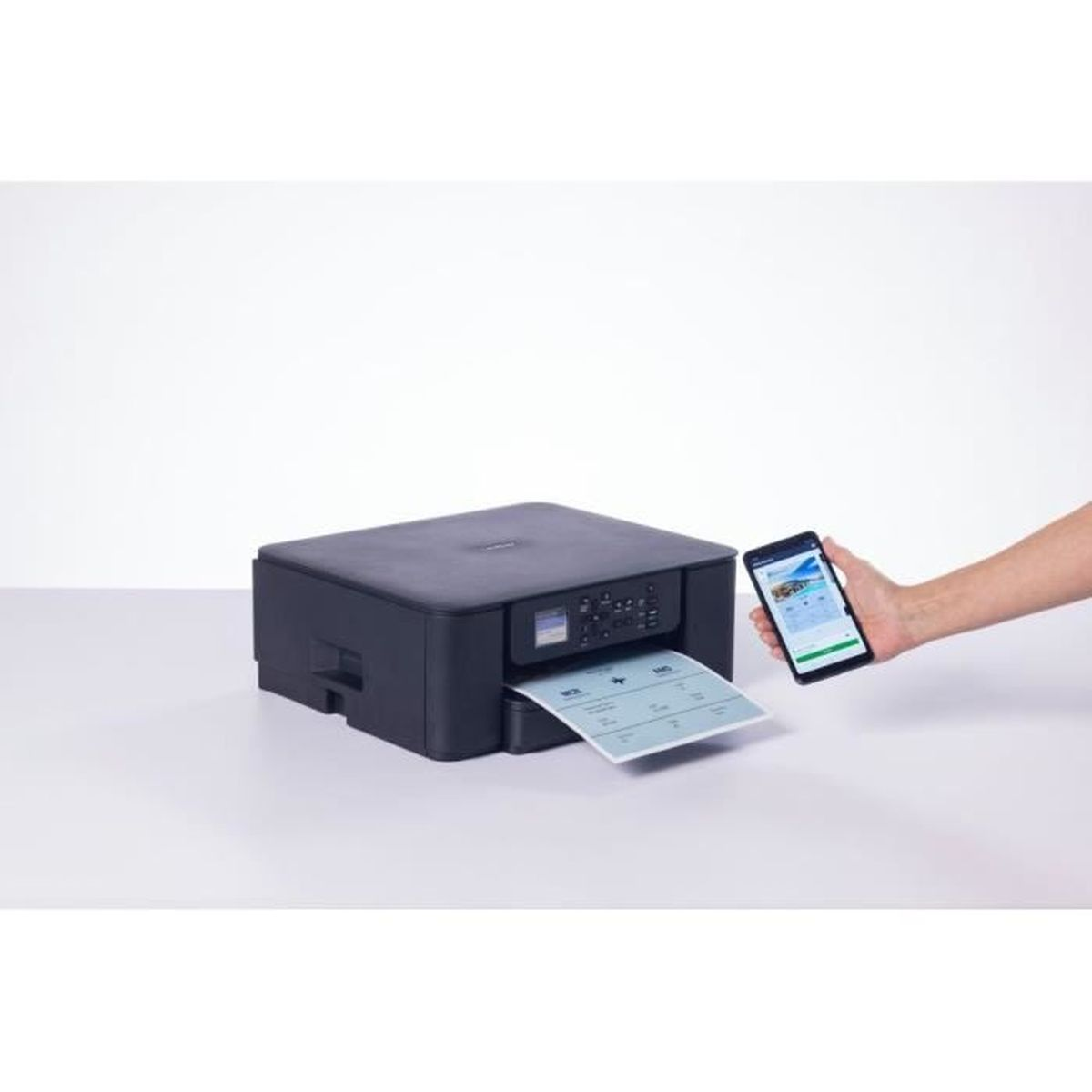 Czarna drukarka drukuje kartkę papieru, podczas gdy ręka trzyma smartfon.