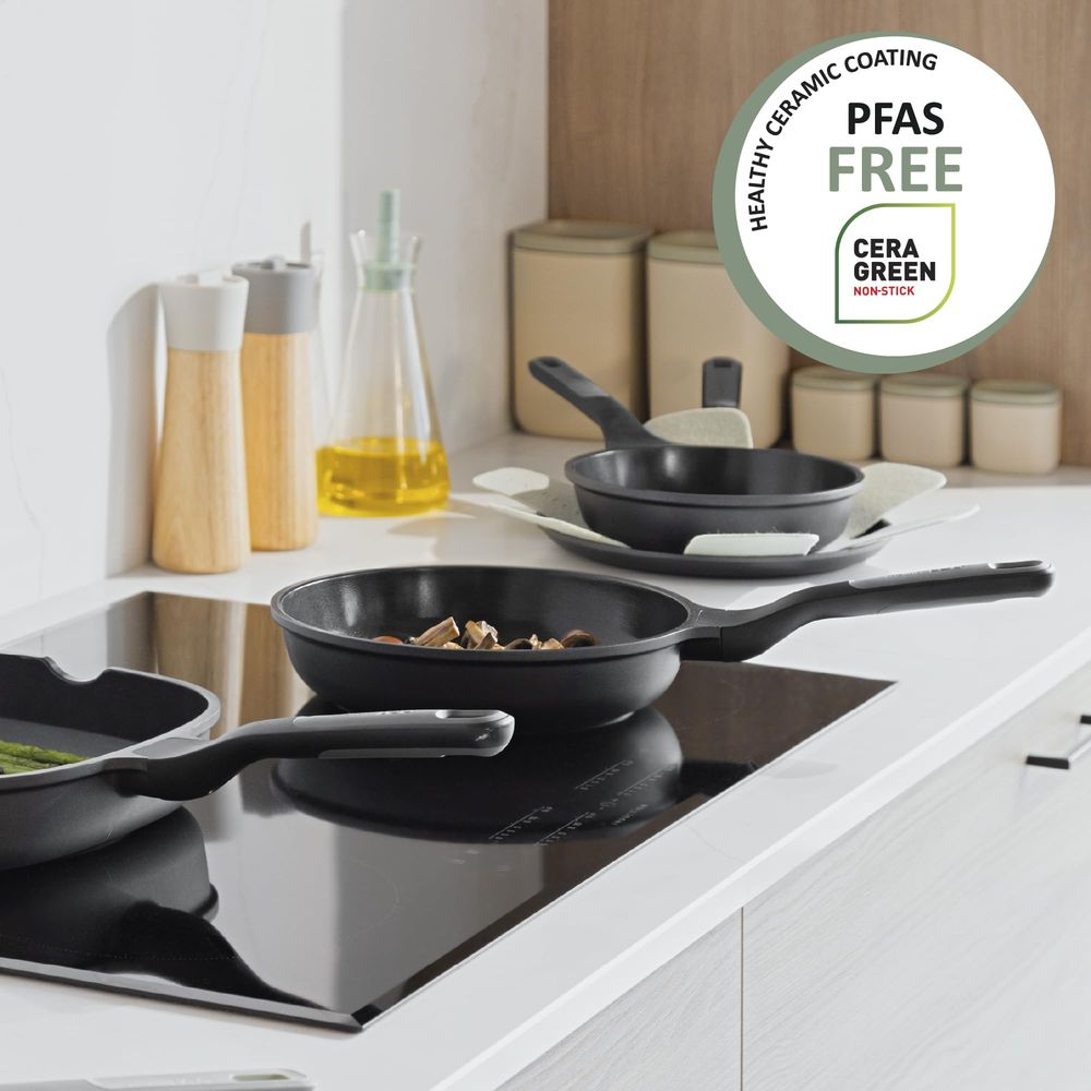 Black frying pans on an induction hob. One pan contains food. A logo says PFAS FREE.