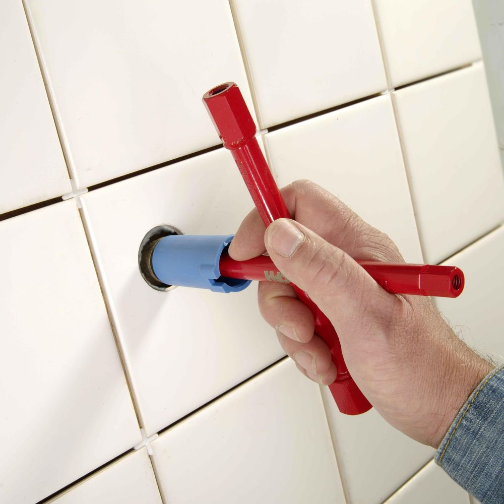 Eine Hand hält ein rotes Werkzeug, das in eine blaue Halterung eingeführt wird, vor einer weißen Kachelwand.