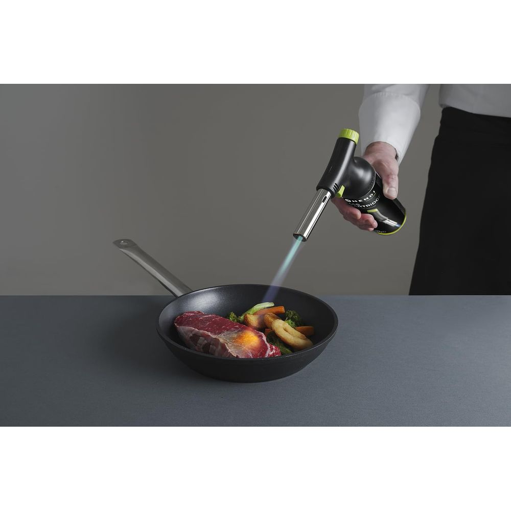 Uno chef usa una fiamma di torcia da cucina su una bistecca e verdure in una padella.