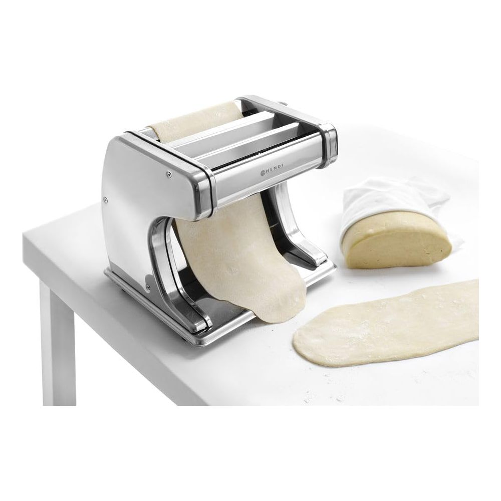 Eine silberne Nudelmaschine mit ausgerolltem Teig und einem Teigklumpen.