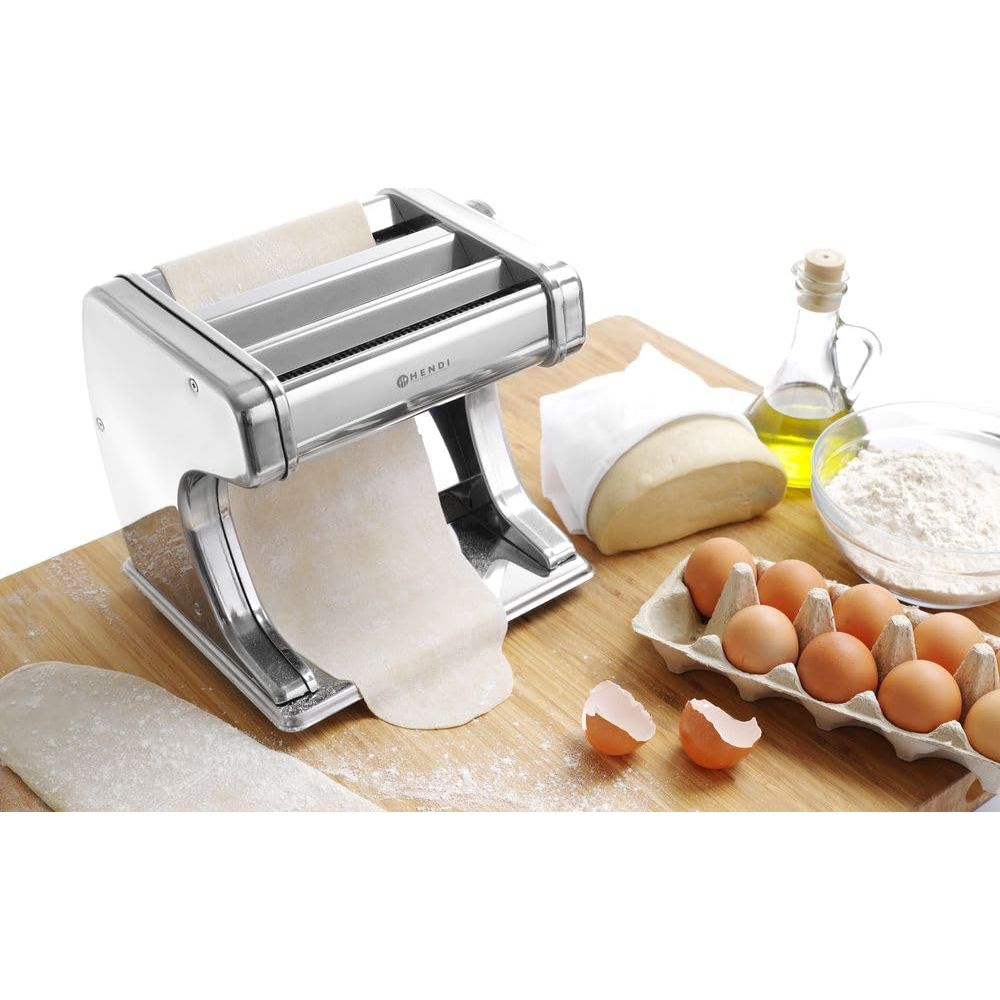 Nudelmaschine mit Teig, Eiern, Mehl und Öl auf einem Holzbrett.