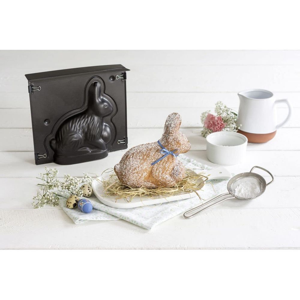 Hasenform, Osterlamm mit Puderzucker, Eier und Backutensilien auf Holztisch.