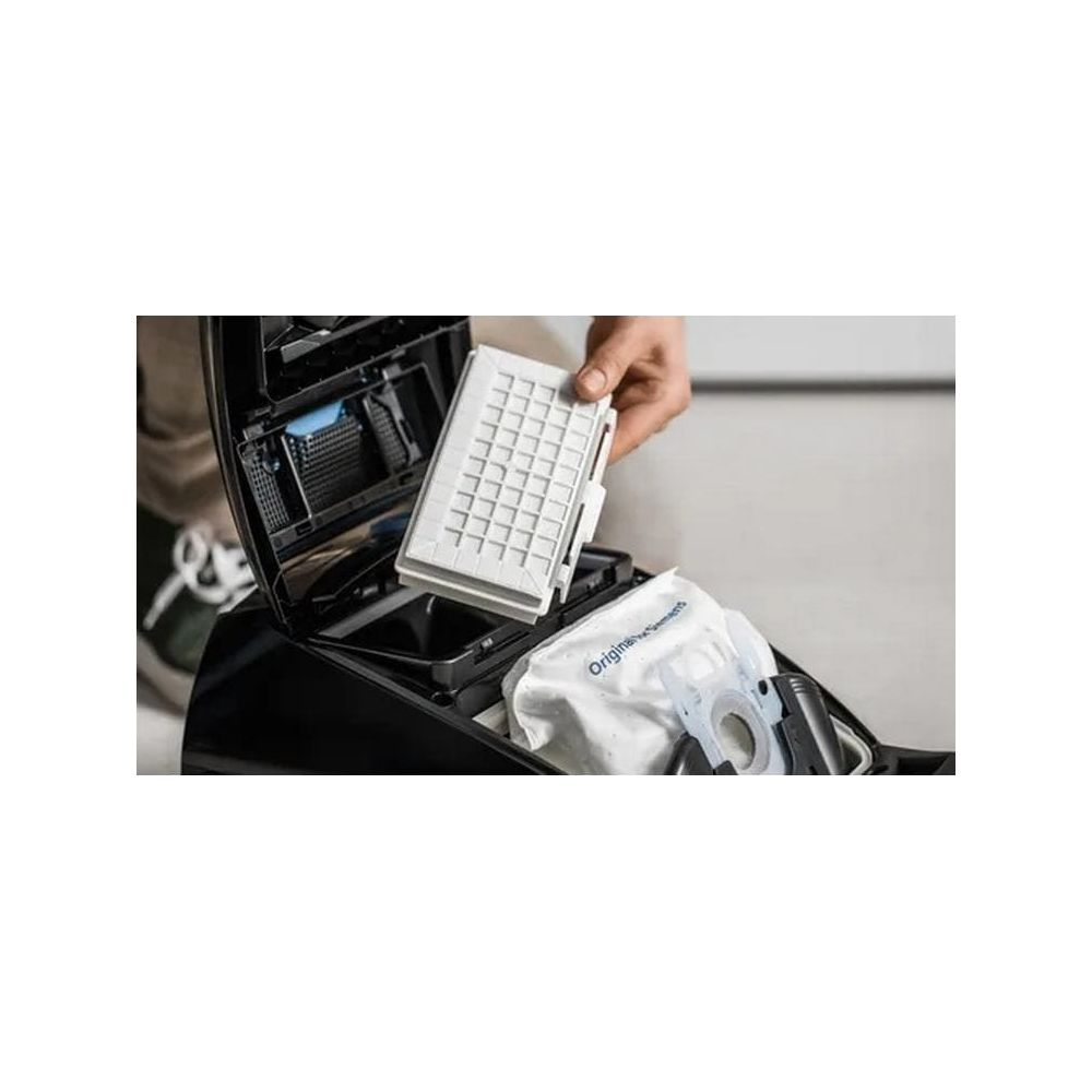 Ręka trzyma biały filtr nad odkurzaczem z workiem w środku.